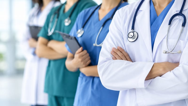 A line of doctors and nurses in white coats and scrubs, clipboards in hand