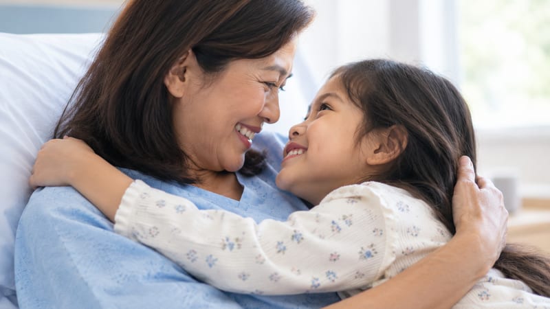 A mother and her young daughter holding each other on a hospital bed
